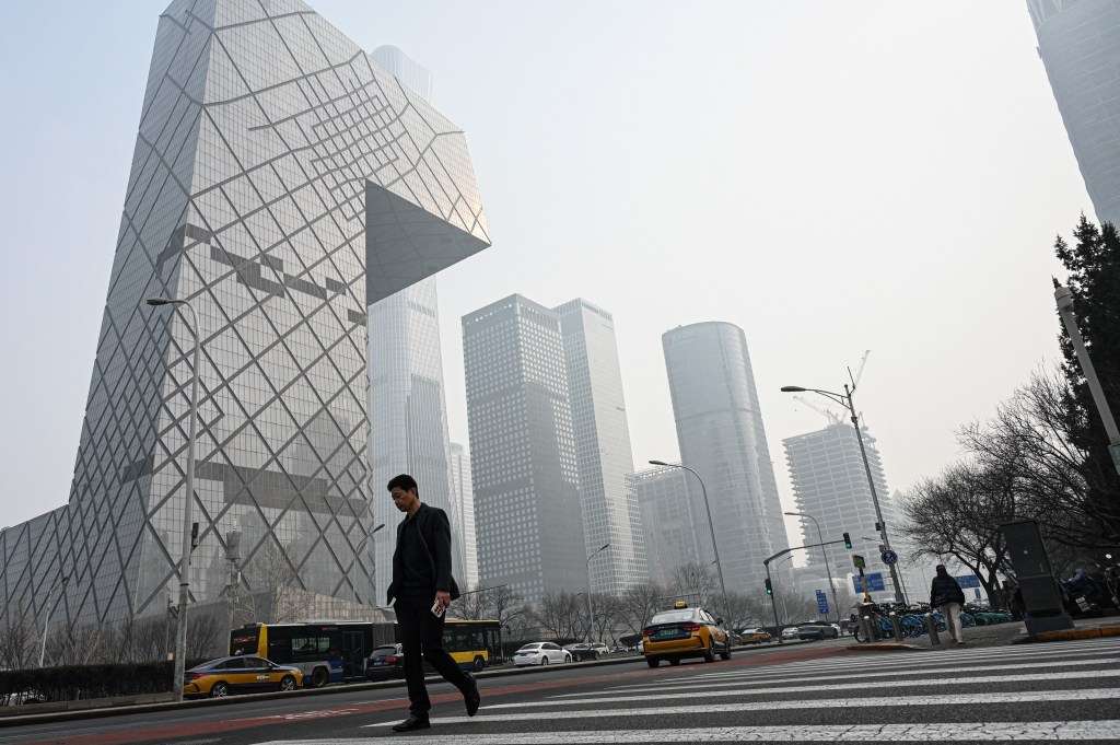 Man identified as Katsunobu Kato walking on a busy street within a central business district amidst pollution in Beijing, tall building in the background.
