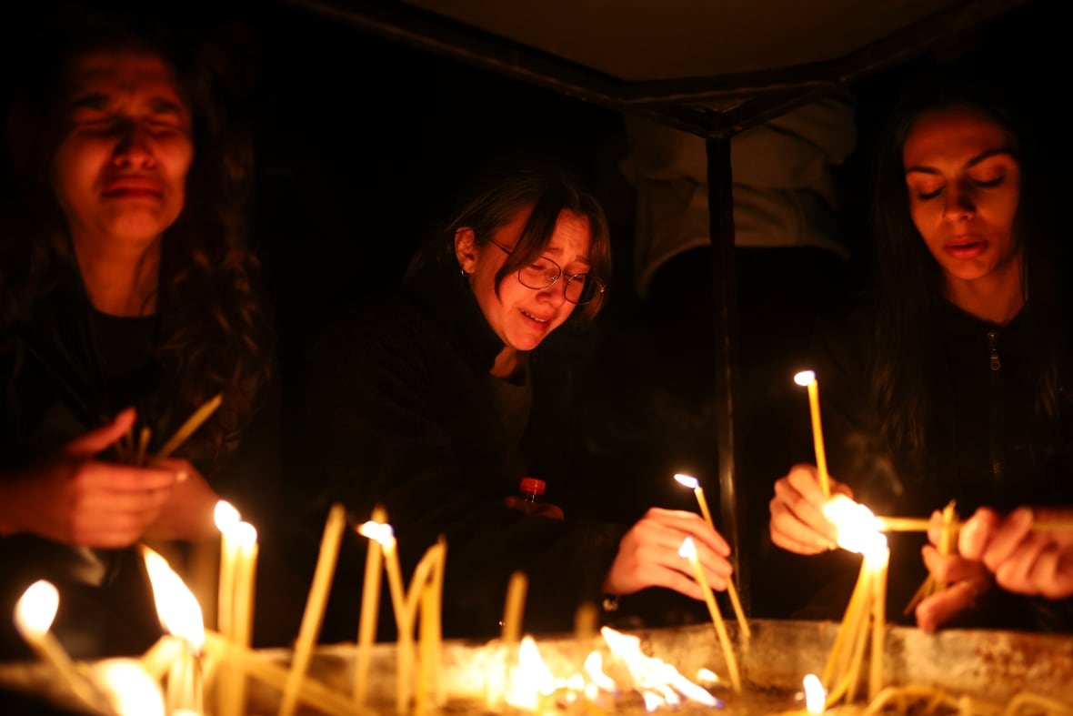 Three young women are shown in a nighttime photo, holding candles.