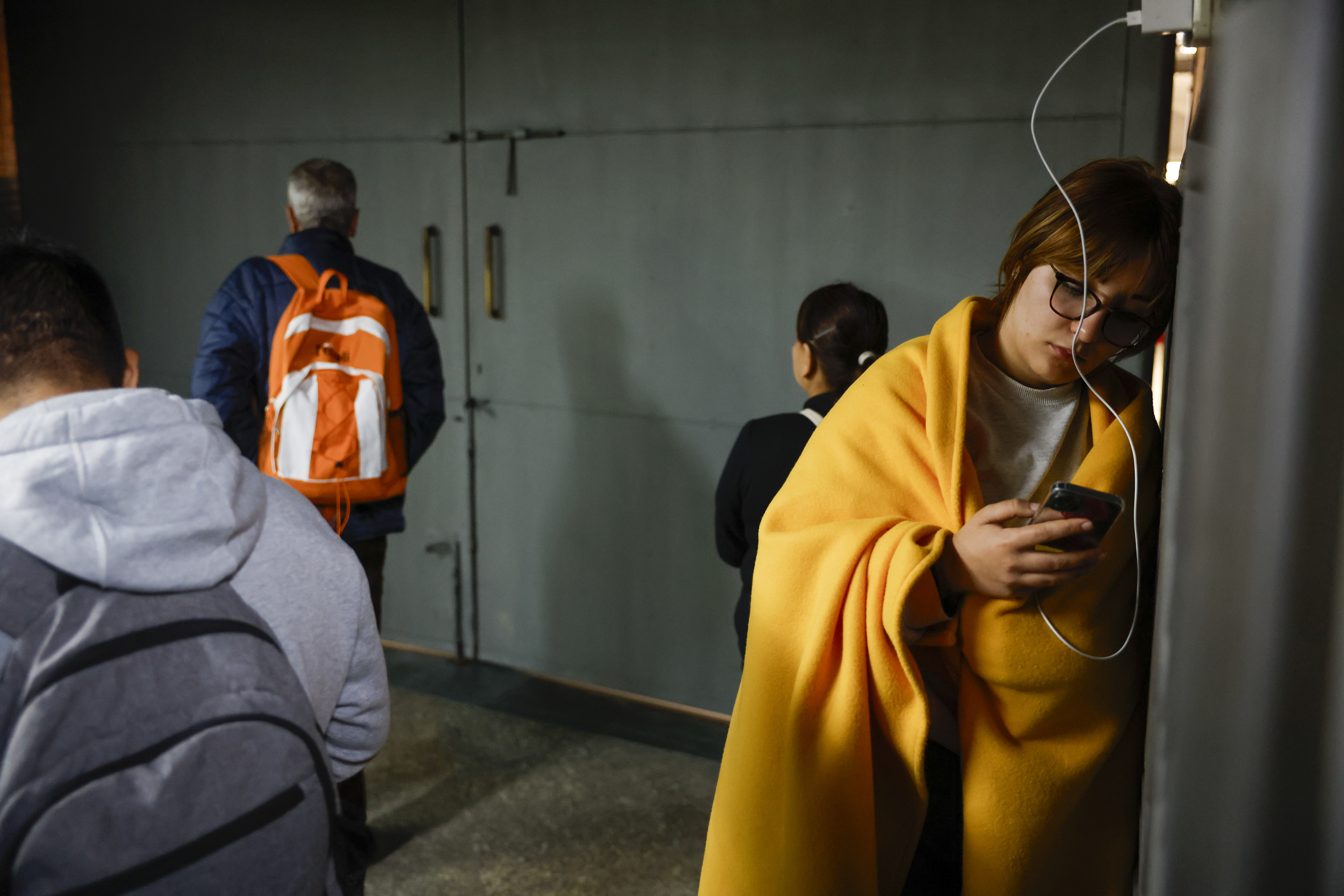 People wrapped in blankets wait at a train station after a widespread power outage.
