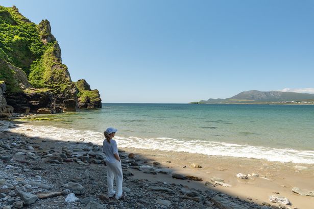 A shot of a young woman in white looking at the ocean from the Keel Beach on Achill Island, Ireland