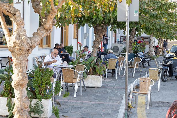 People at a coffee in Ikaria island. Sunny autumn day in Evdilos Village in Ikaria. Panoramic view of the traditional picturesque fishing village with the wooden boats in the harbor, one of the most popular holiday destination on the Greek island of Ikaria that is located in the Aegean Sea. The Mediterranean Icaria island is famous for the longevity, human connection and the alternative simplified lifestyle closer to nature. The settlement of Evdilos is at the North of the island and is built amphitheatrically around the natural bay. Evdilos was built after 1830, when the fear of the pirates stopped raiding. Nowadays about 500 inhabitants live in here while most of whom are engaged in fishing and tourism. The village consists of picturesque alleys and traditional mansions and neoclassical buildings with unique architecture. Streets are ornated by many flowers and well-cared gardens. Evdilos is considered a popular tourist resort. Accommodations like hotels, rooms to let, apartments, cafes, bars, mini markets, banks, car rental and excellent fish taverns and restaurants among other shops are available in Evdilos. There is no beach in Evdilos except a small spot of sand and pebbles near the port, used for sunbathing and swimming by locals and tourists but large sandy beaches and coves are nearby. Ikaria Island, Greece on November 2022 (Photo by Nicolas Economou/NurPhoto via Getty Images)