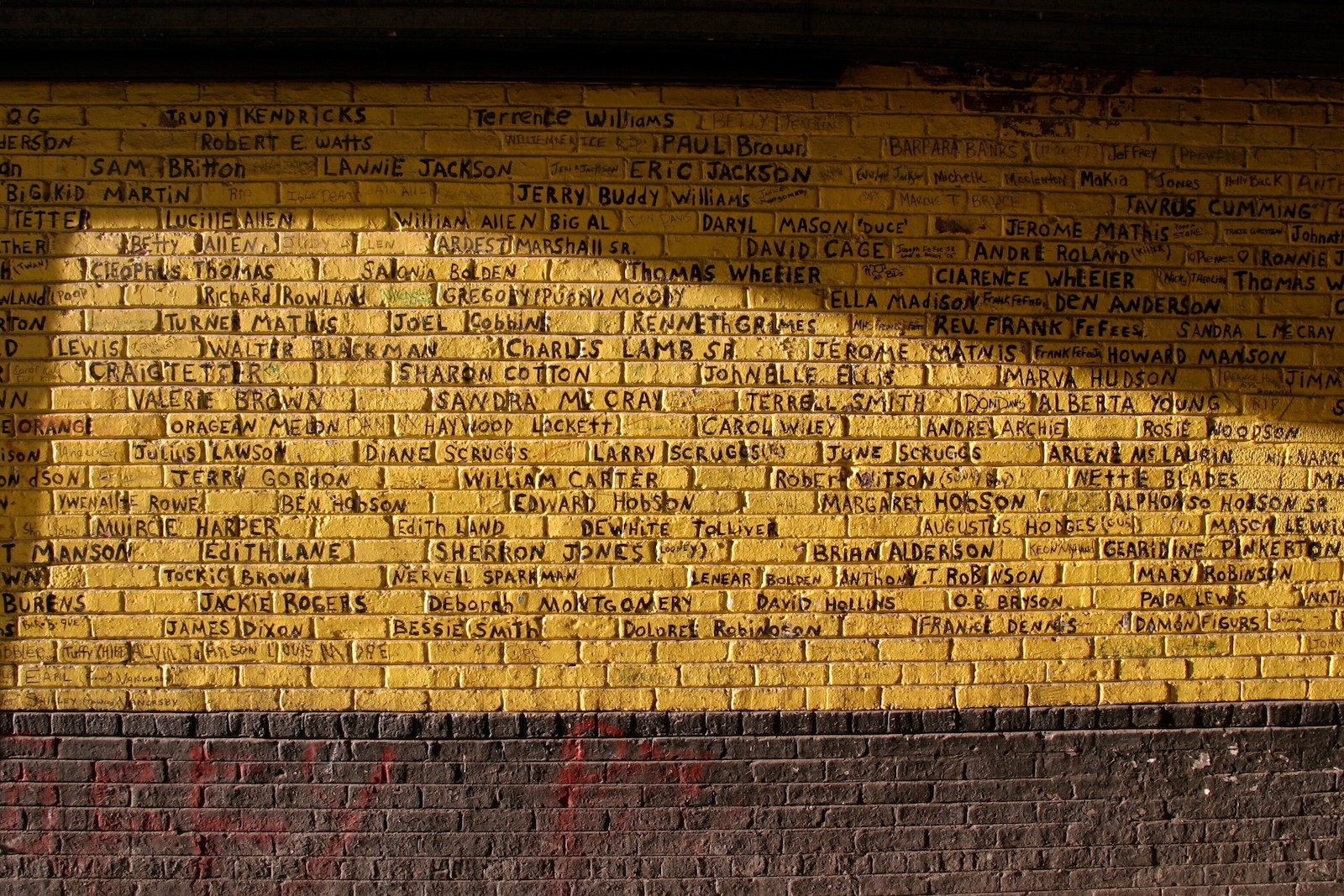 A brick wall painted yellow with names written on it.