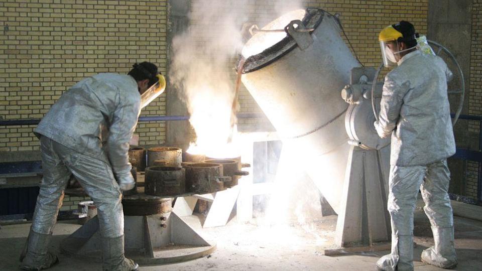 Technicians work inside of a uranium conversion facility, appearing in white overalls and pouring liquids into containers, on 30 March 2005 just outside the city of Isfahan, Iran