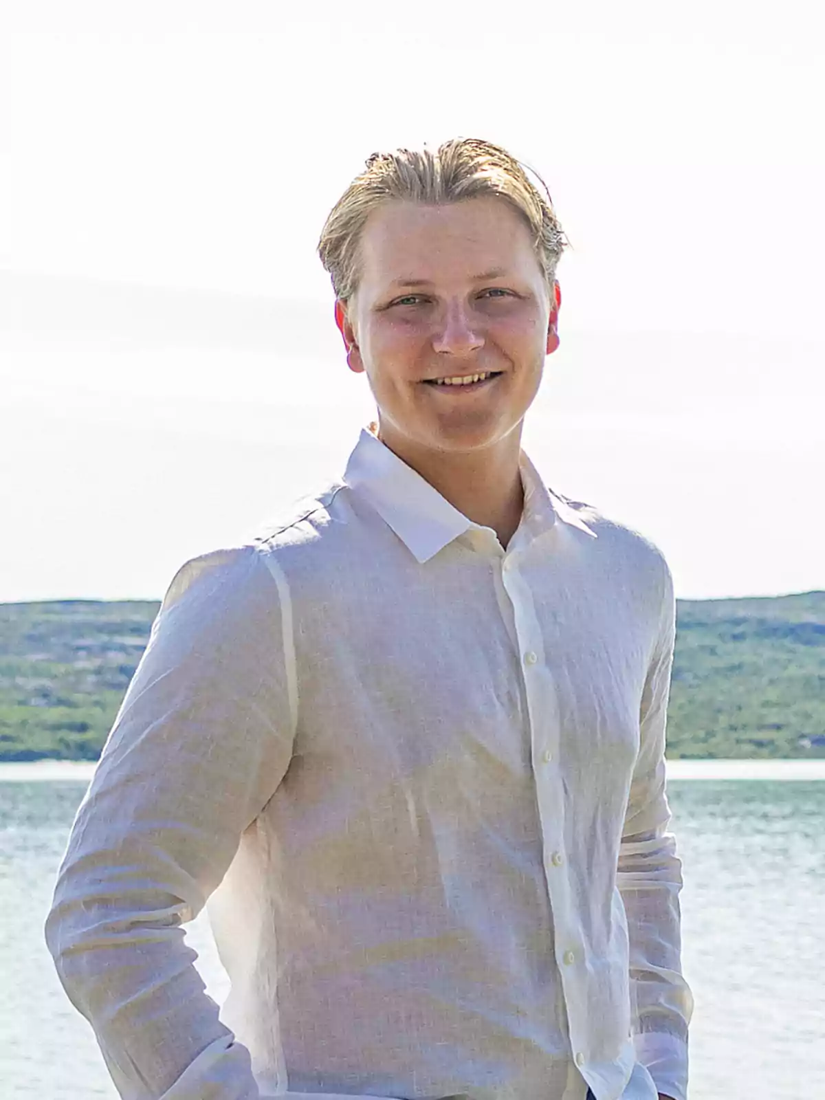 Sverre of Norway in a white jersey smiles in front of a landscape of water and hills.
