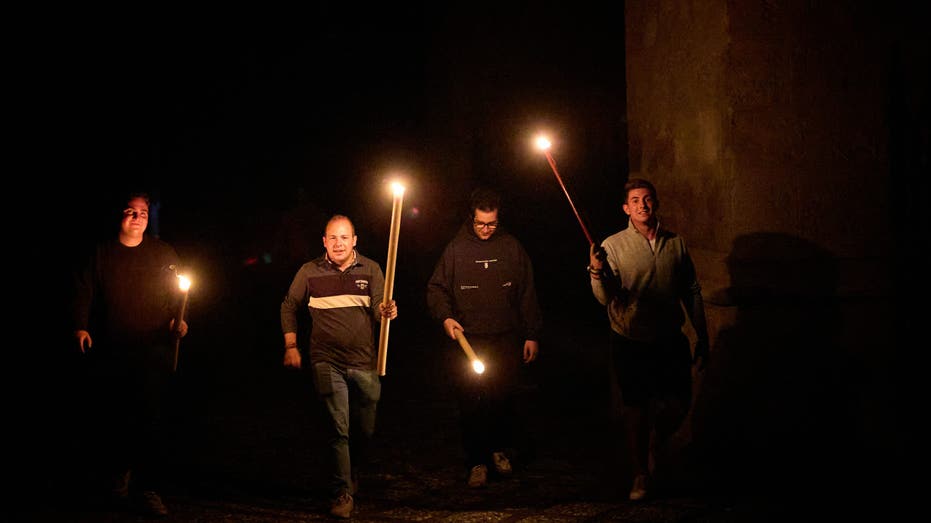 A group of people walks down the street with large, lit candles