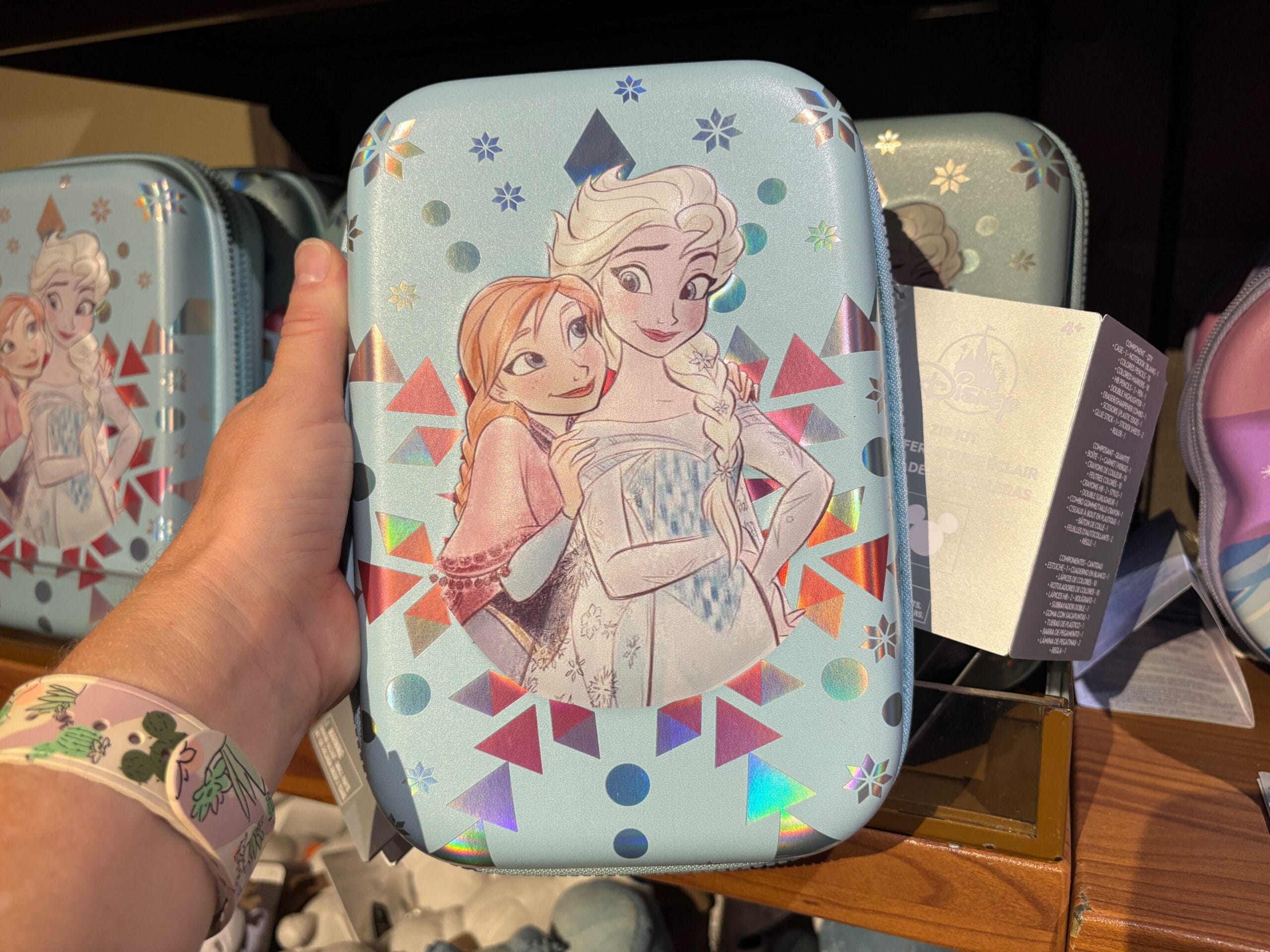 A hand holds a Frozen-themed case featuring Anna and Elsa with colorful geometric designs on a light blue background.