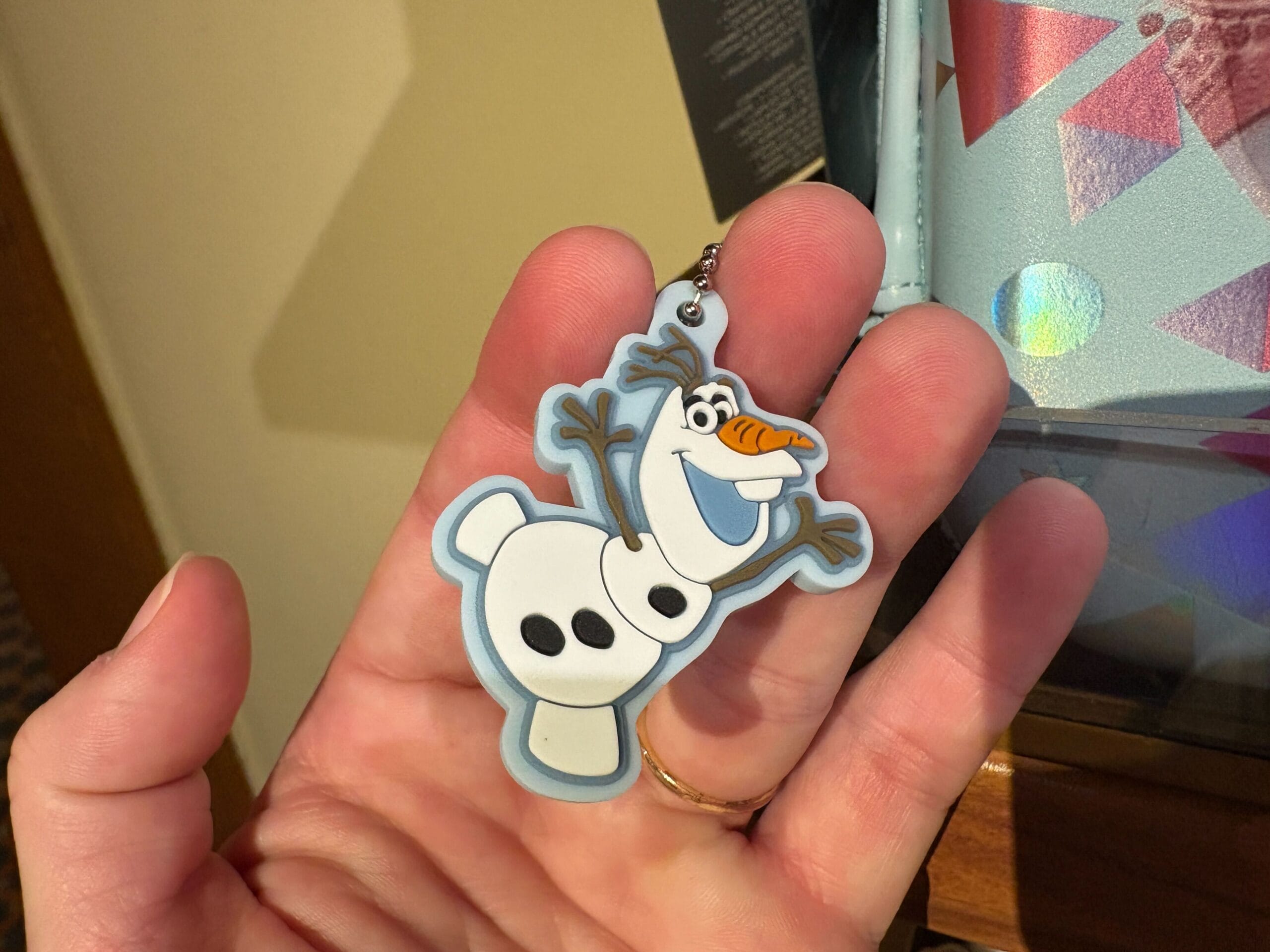 A hand holds a keychain of Olaf, the snowman character from the movie "Frozen," smiling with arms raised.