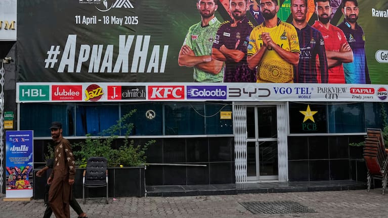 Workers walk past an advertisement board of Pakistan Super League Twenty20 tournament with the pictures of cricketers, installed at the Rawalpindi Cricket Stadium
