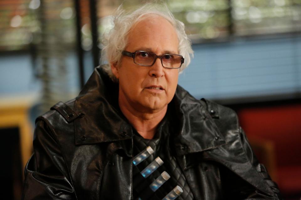 I don't know who this is, but they are wearing a leather jacket over a sci-fi inspired outfit, sitting indoors with a serious expression