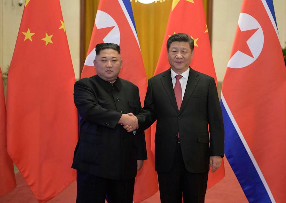 Two men shake hands in front of flags.