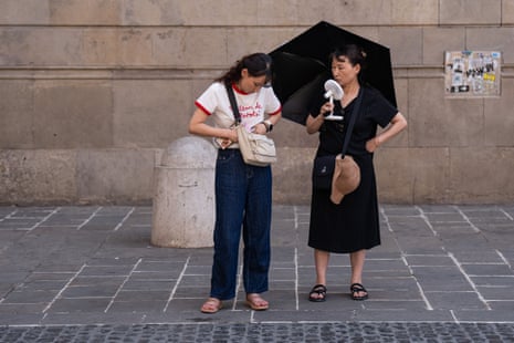 Tourists stroll through the city center during the middle of the day, carrying handheld fans, hats, sunglasses, and water bottles to combat the persistent heat, in Barcelona, Spain.