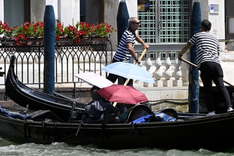 Tourists protect themselves from the sun with umbrellas during a gondola ride in Venice lagoon.