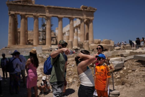 A man tries to cool a girl with water during their visit to the Parthenon temple atop the Acropolis hill, as a heatwave hits Athens, Greece.
