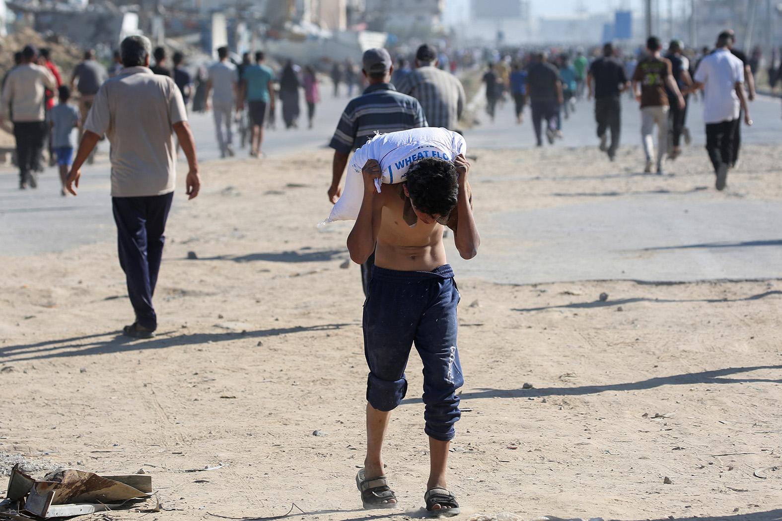 A displaced Palestinian youth ferries a bag of food aid on his shoulders after people stormed a World Food Programme warehouse in Deir el-Balah in the central Gaza Strip on May 28. Photo: Eyad Baba/AFP