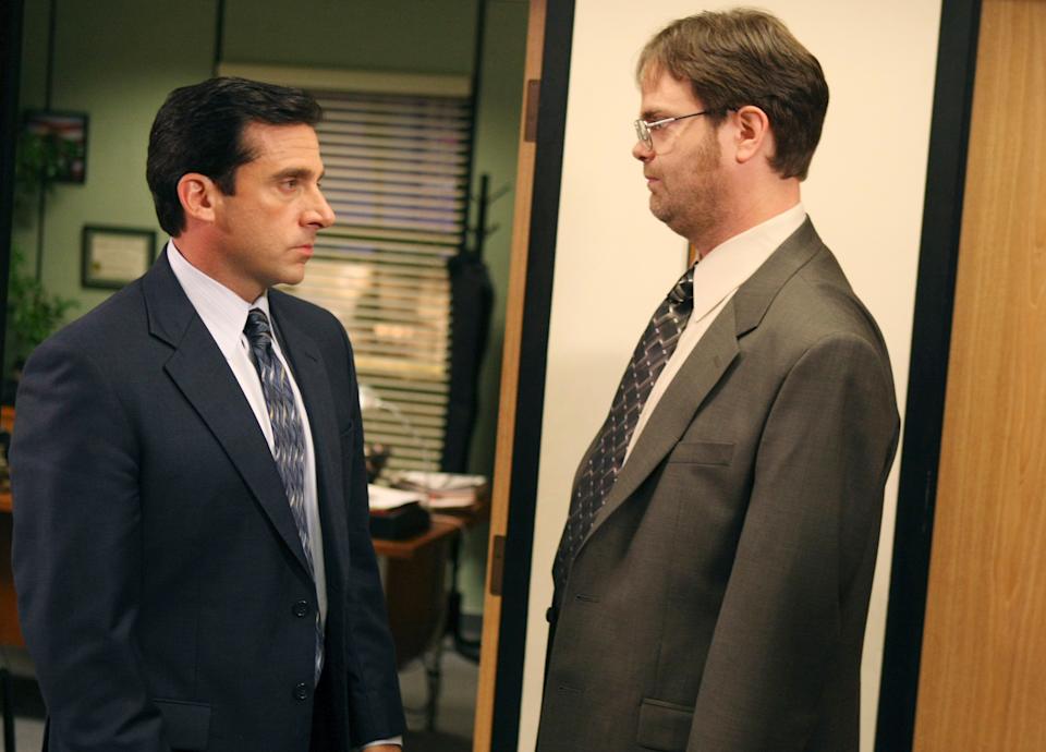 Two men in business suits face each other in an office setting, expressing a serious mood