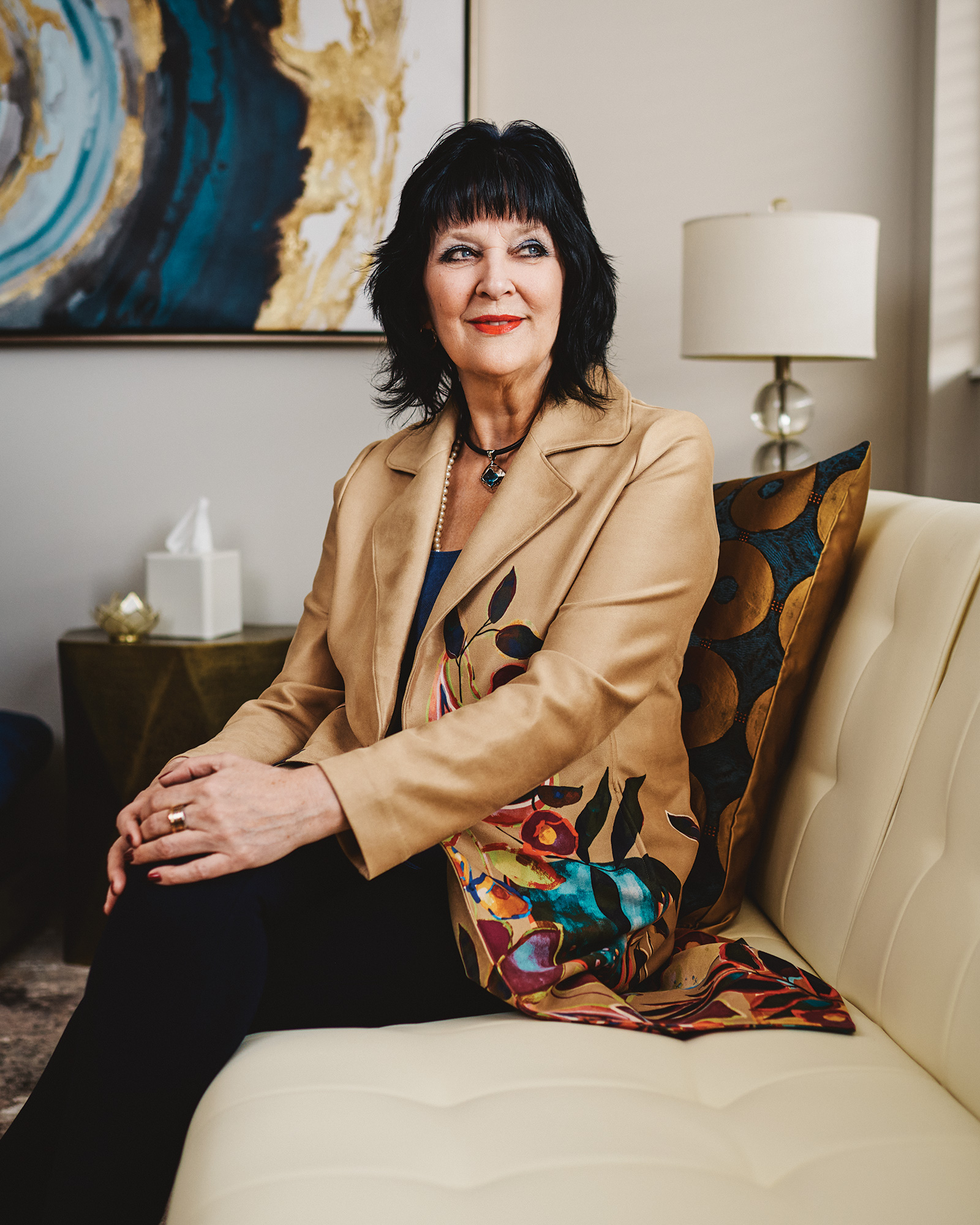White woman with short black hair sits cross-legged on a couch