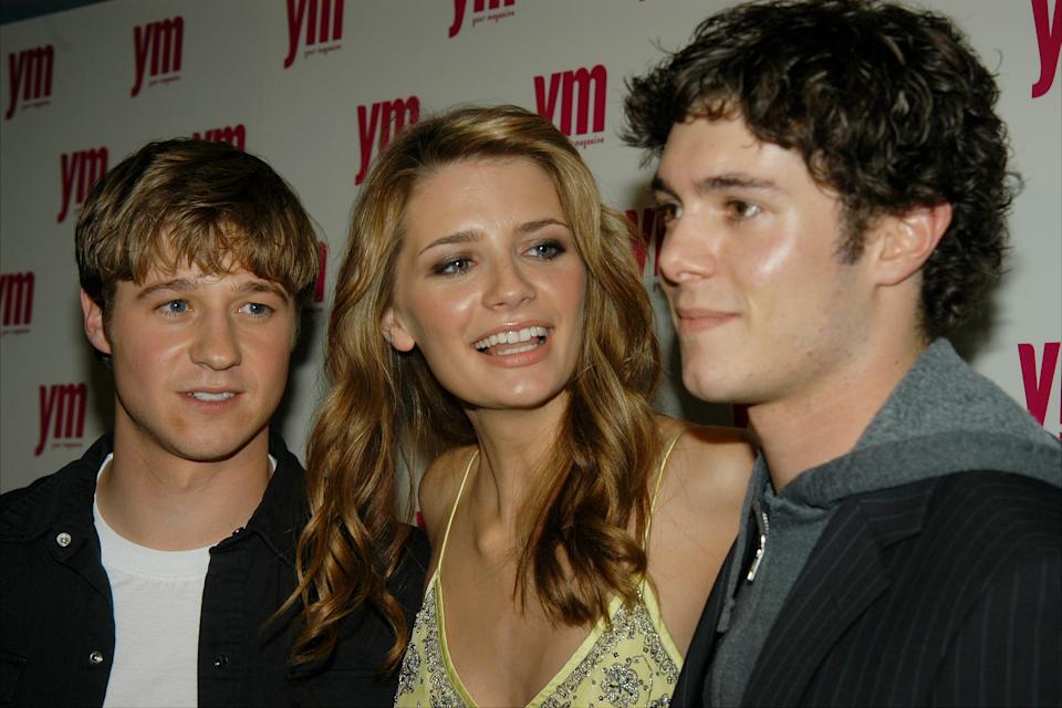 Three people at a YM event; a woman in an elegant summer dress, and two men, one in a casual jacket and the other in a hoodie