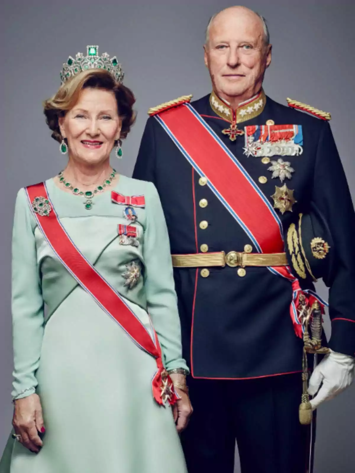 Queen Sonja and King Harald of Norway dressed in formal attire and decorations, the woman wearing a tiara and a light green dress, while the man wears a dark military uniform with medals and a red sash.