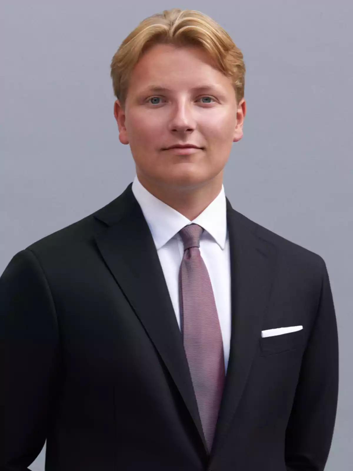 Sverre of Norway in a dark suit posing against a gray background.