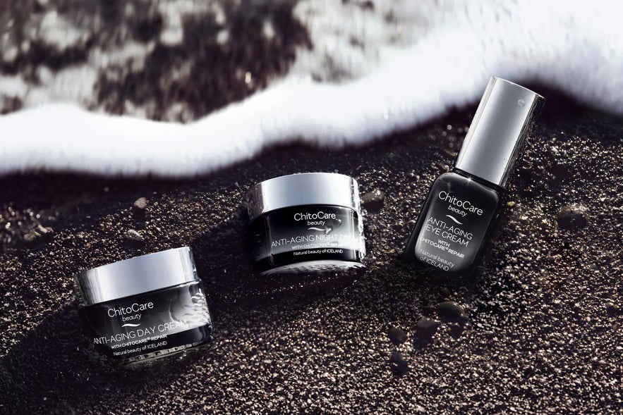 ChitoCare Beauty anti-aging day, night, and eye creams are displayed on black sand with a gentle ocean wave.