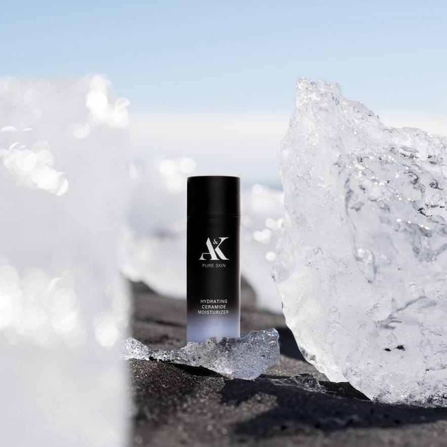 AK Pure Skin Hydrating Ceramide Moisturizer bottle on black sand, surrounded by sparkling ice formations.