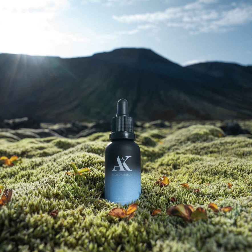 AK Pure Skin Face Oil Serum bottle rests on vibrant green moss against a backdrop of mountains in Iceland.
