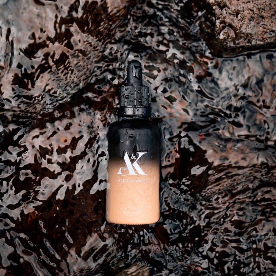 AK Pure Skin Face Tan Water bottle with a gradient design, submerged in clear, rippling water.
