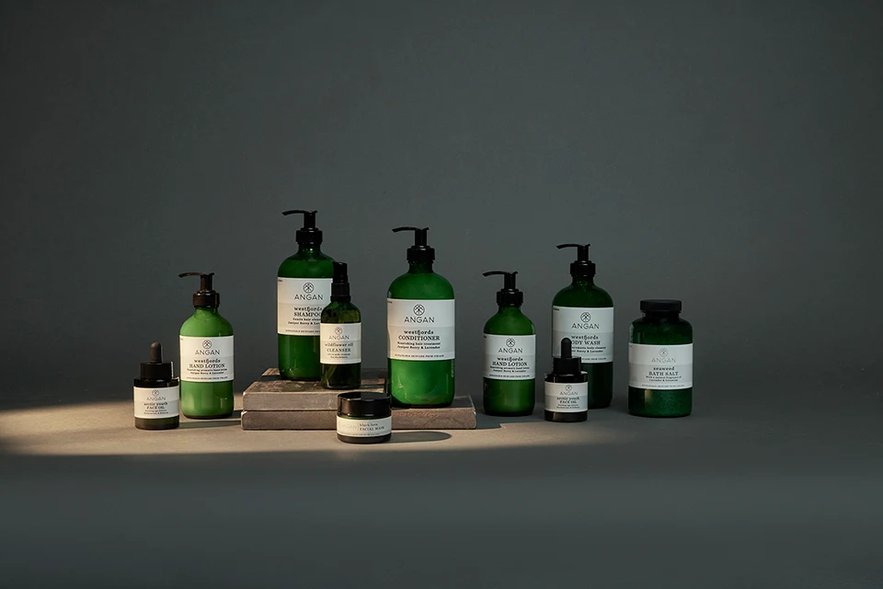 A curated collection of Angan Skincare products in green bottles and jars are neatly displayed.