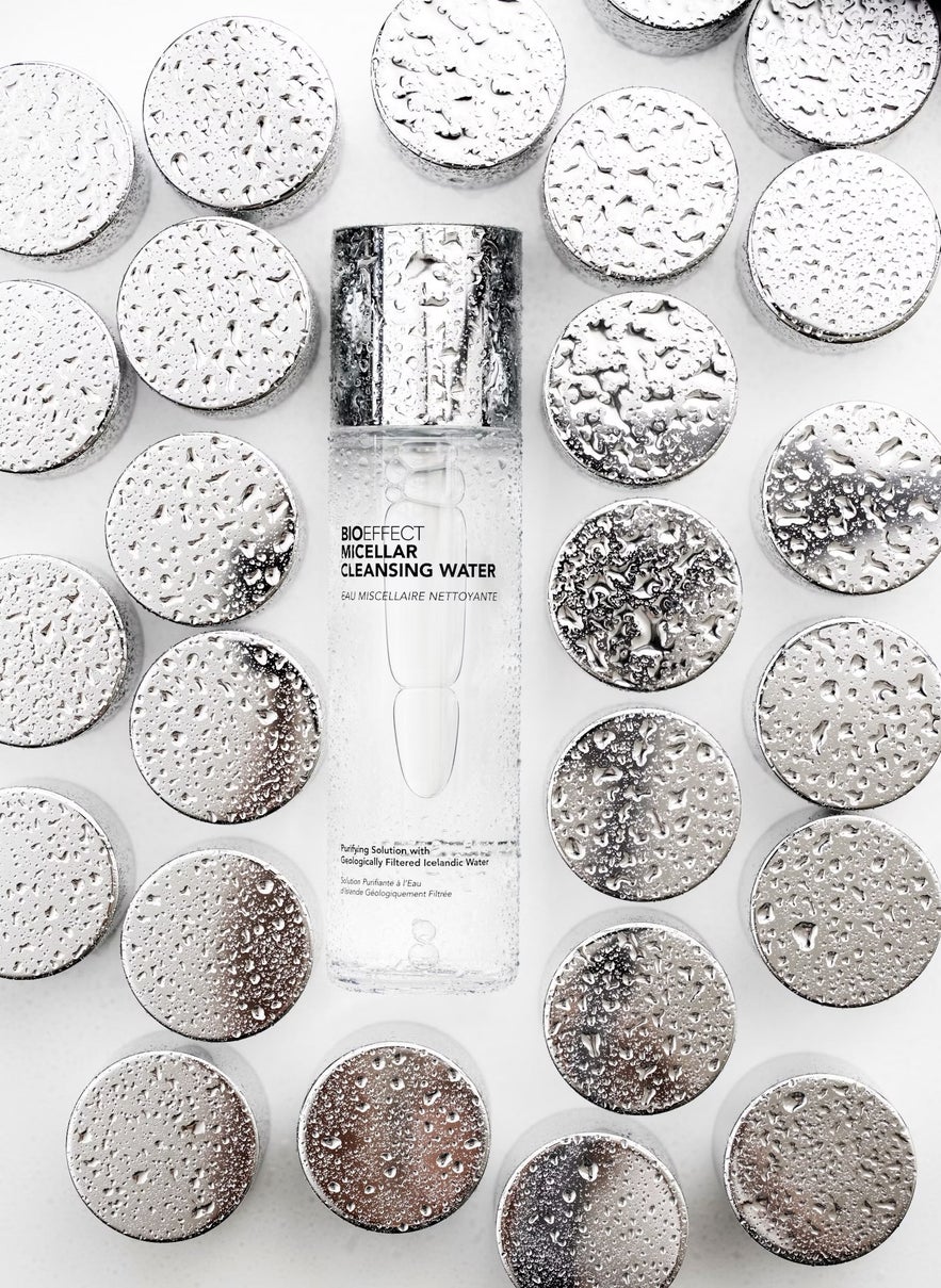 A bottle of BIOEFFECT Micellar Cleansing Water is surrounded by wet, reflective silver lids on a white surface.
