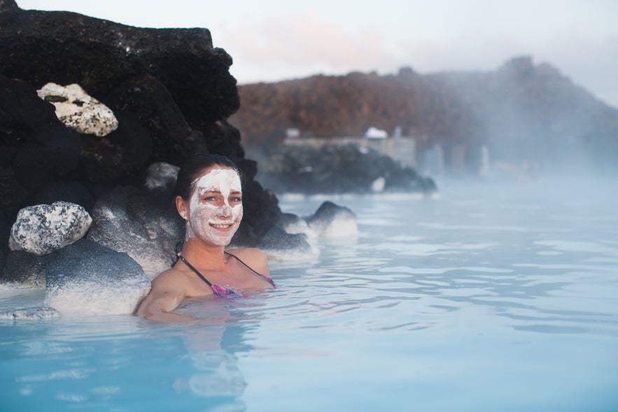 A woman with a white mud mask relaxes in the warm, milky-blue waters of Iceland's Blue Lagoon