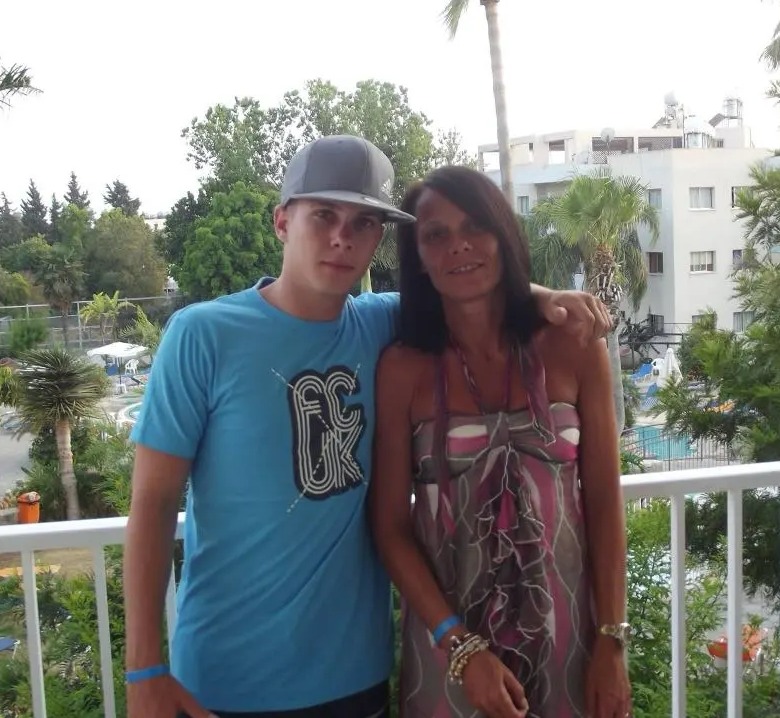 A young man and woman stand on a balcony, smiling.