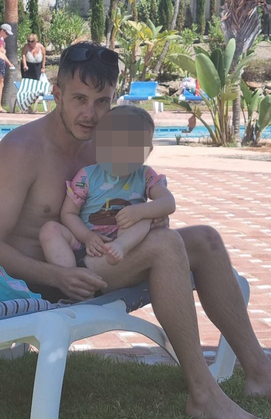 Man holding a toddler by a pool.