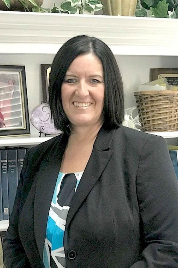 A woman with black hair stands in front of a book shelf.