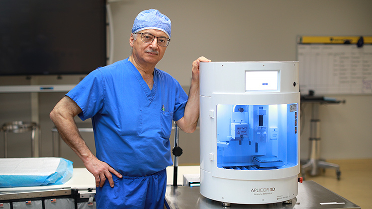 Portrait of Dr. Munier Nazzal, a UToledo Health vascular surgeon, who is posing next to a 3D graft printer.