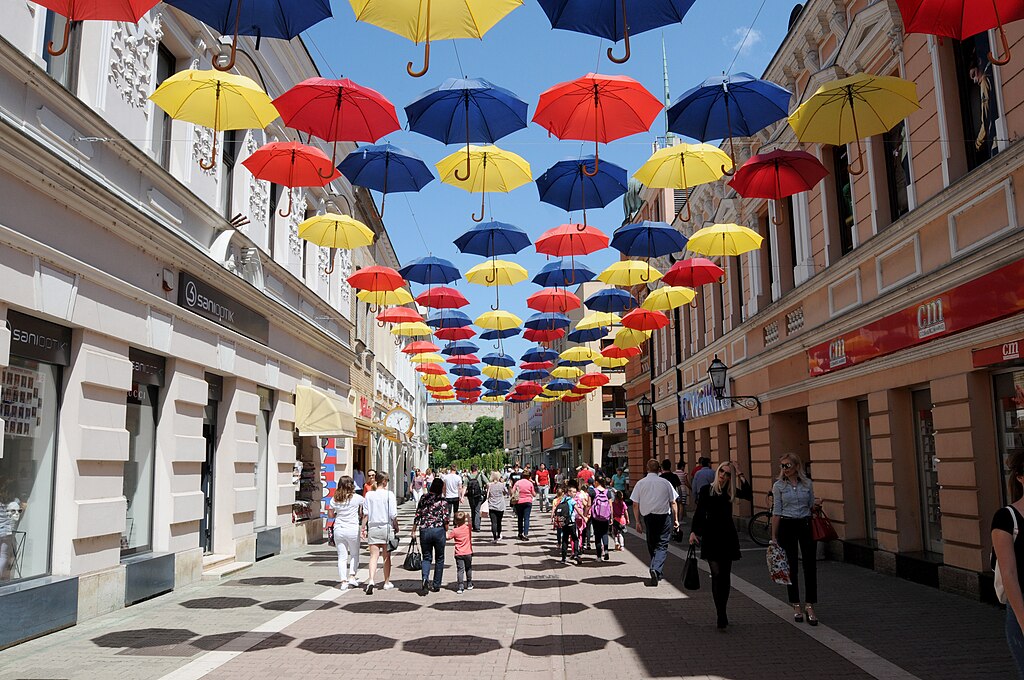 Pedestrians under a public art installation of colorful umbrellas.