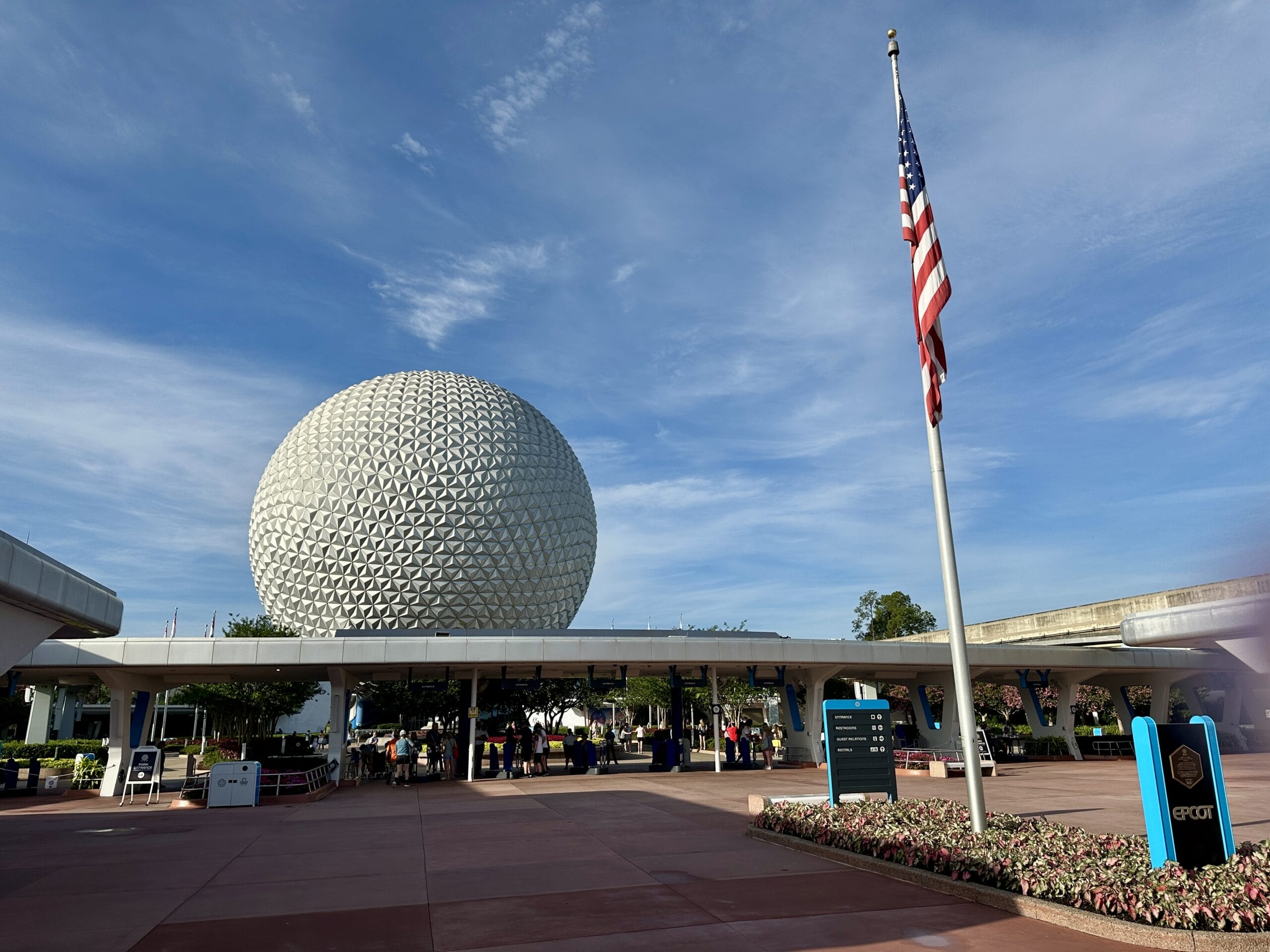EPCOT PHOTO REPORT: Spaceship Earth geodesic sphere with an American flag and visitors under a blue sky.