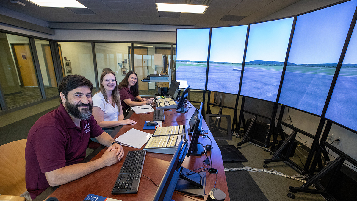 Three people seated in a simulated air traffic control tower.