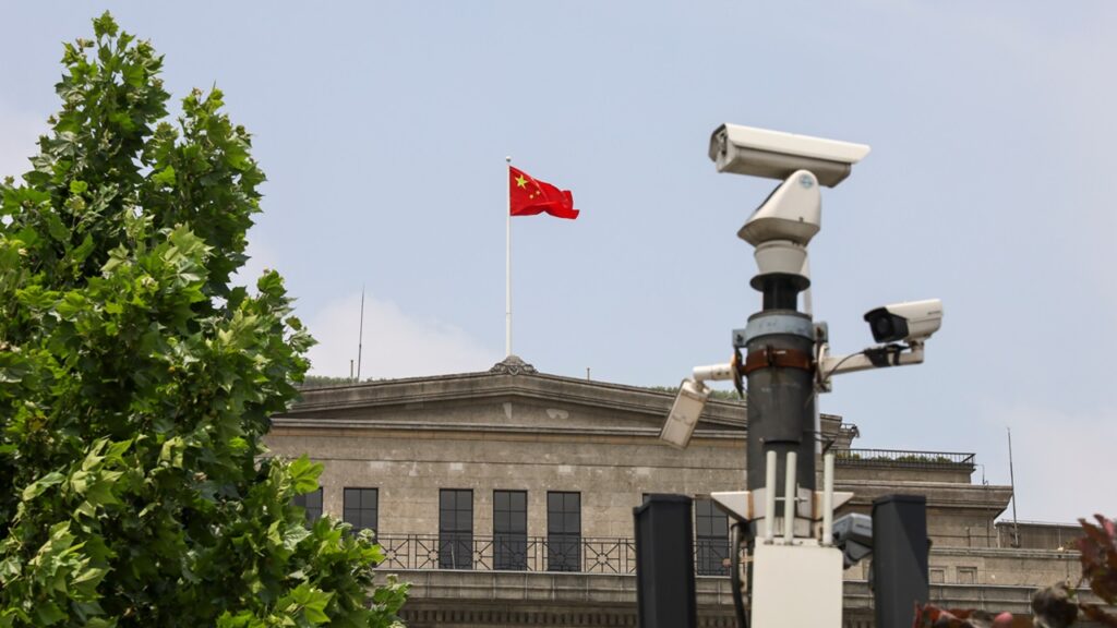 A building with a Chinese flag on it, behind a security camera.