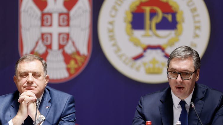 Serbian president, Aleksandar Vučić, and Milorad Dodik, the president of Rerpublika Srpska sit at a table in front of Serb nationalist symbols.