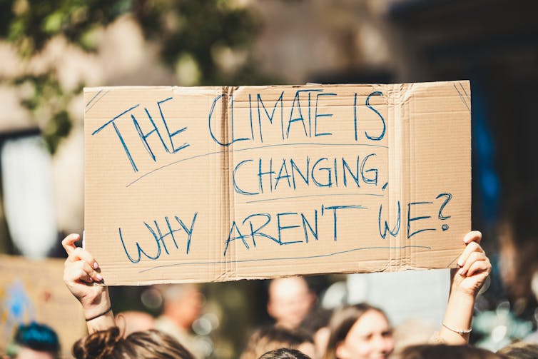 A person holds a sign that reads 'The climate is changing, why aren't we?'