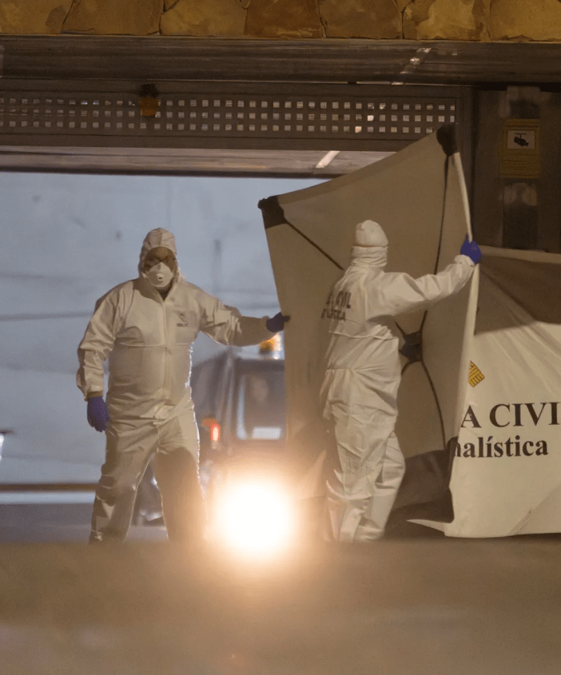 Two forensic officers in hazmat suits handling a body bag.