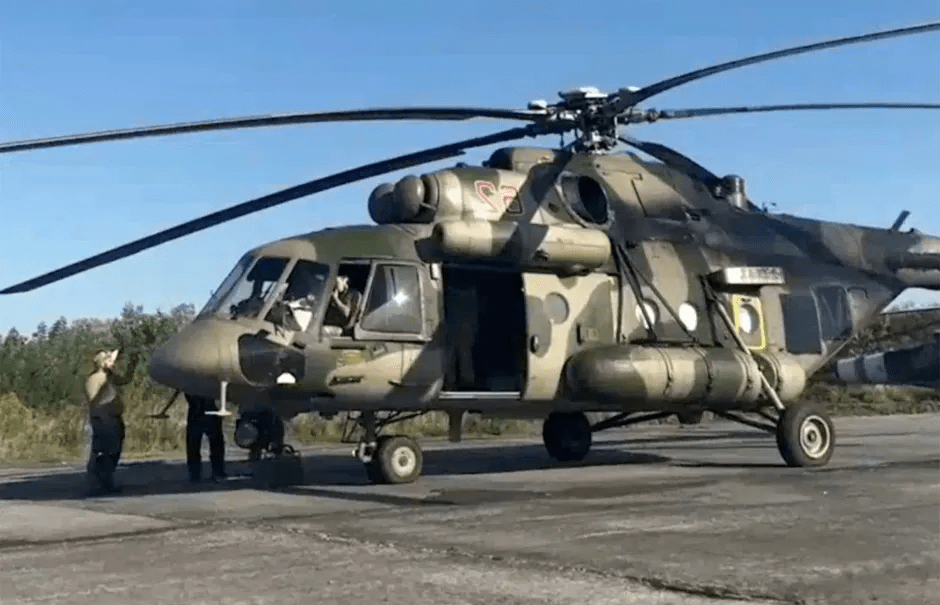 Military helicopter on the ground with people nearby.