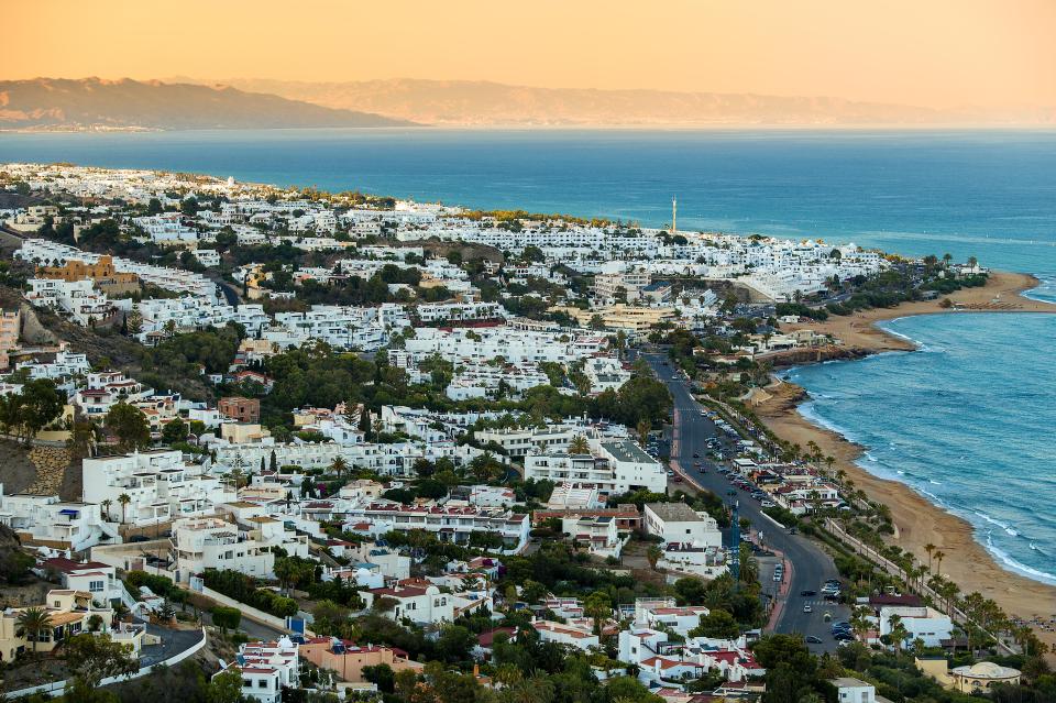 Aerial view of a coastal town with white buildings and a sandy beach.