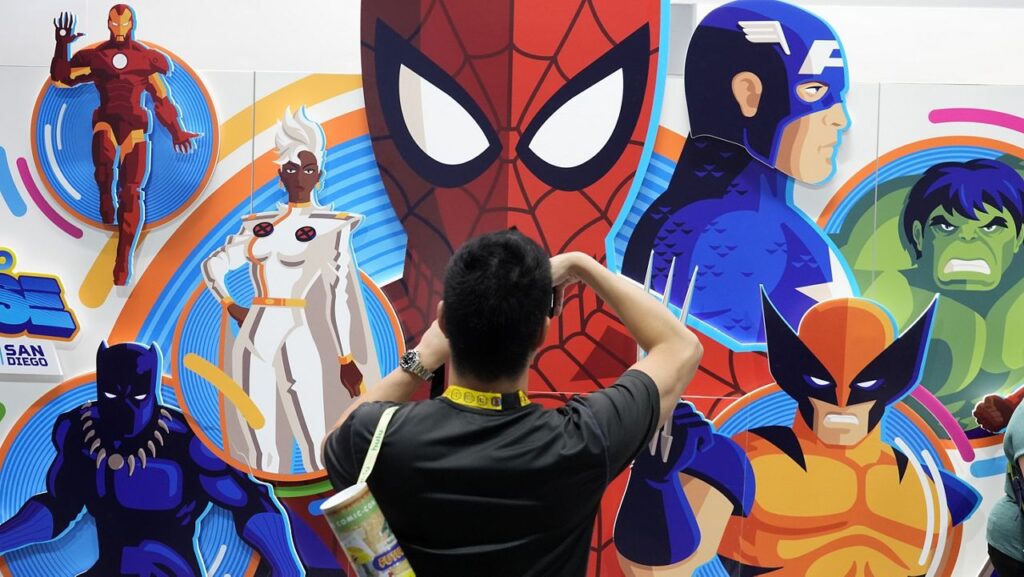 An attendee takes a picture of an illustrated wall of Marvel superhero characters during preview night for Comic-Con International on July 24, 2024, in San Diego. (AP Photo/Chris Pizzello)