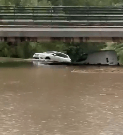 Cars submerged in floodwater under a bridge.