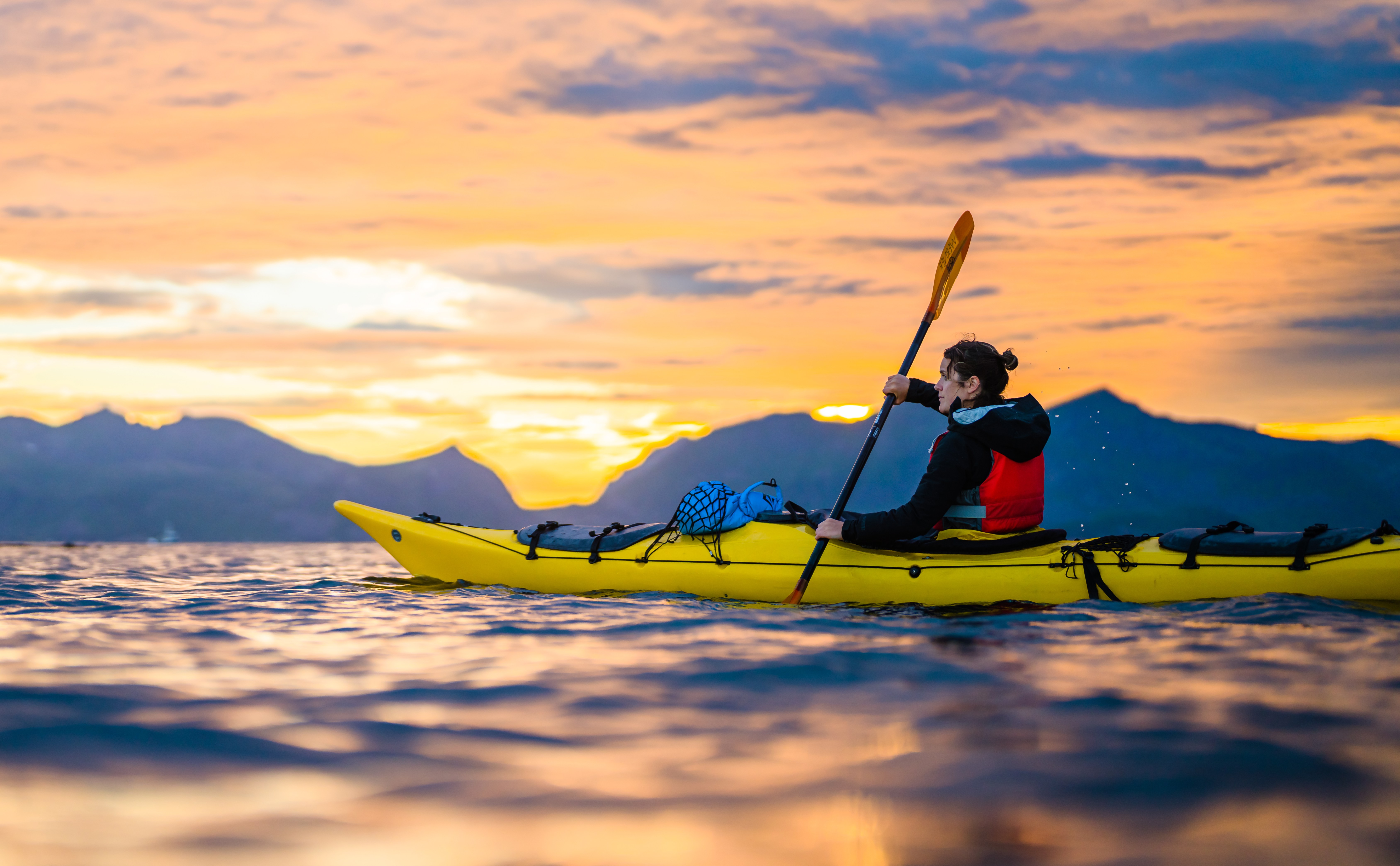 Person kayaking at sunset in Lofoten Islands, Norway.