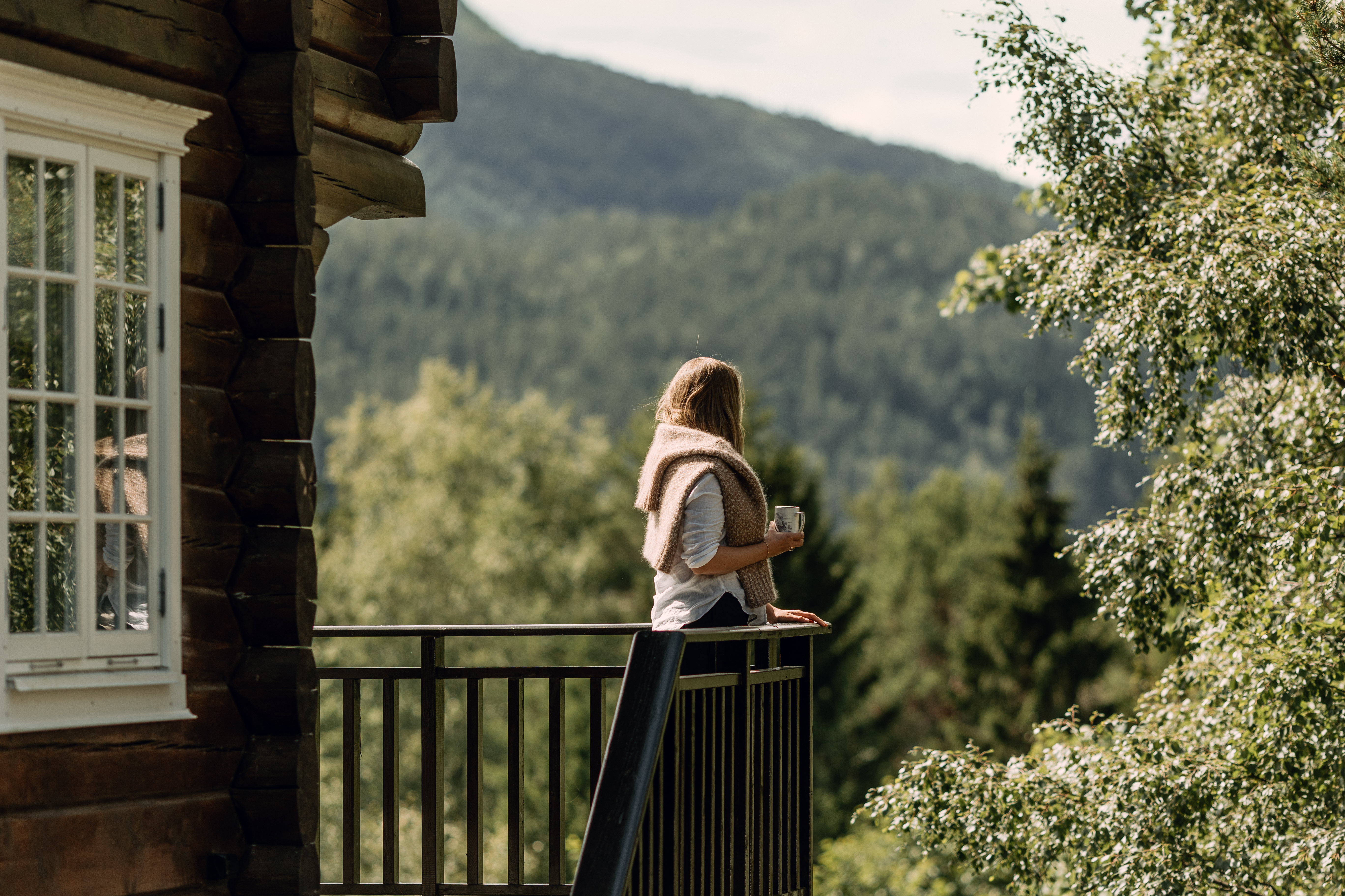Woman enjoying a drink on a balcony overlooking a mountain landscape.