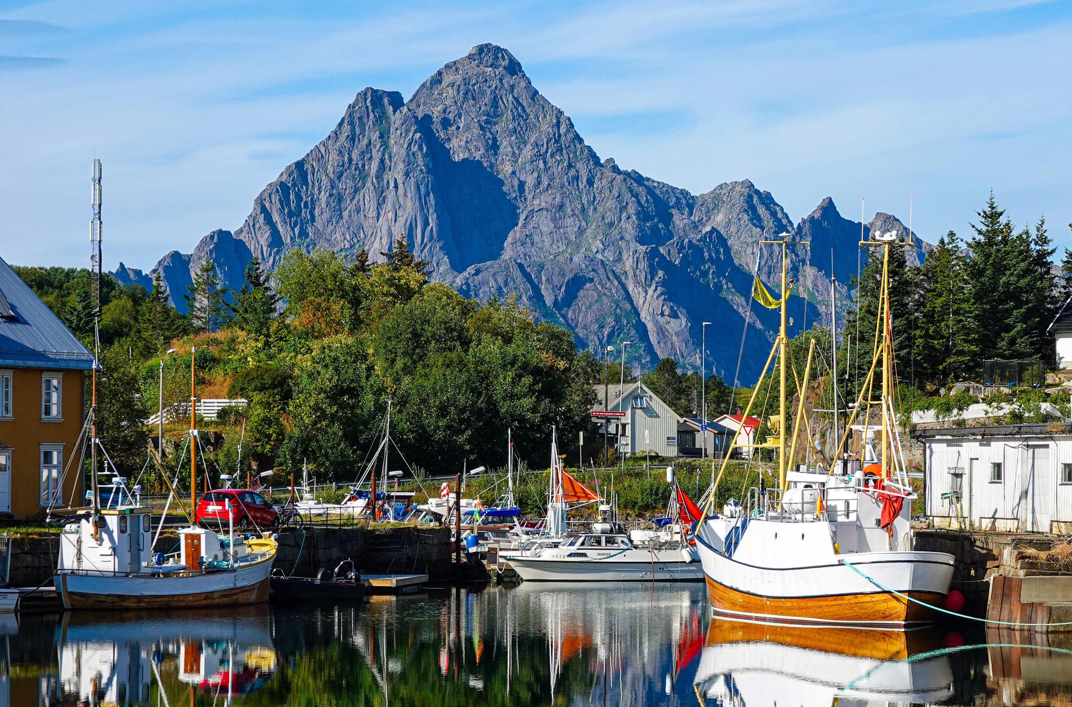 Reflections of boats and mountains in a calm harbor.