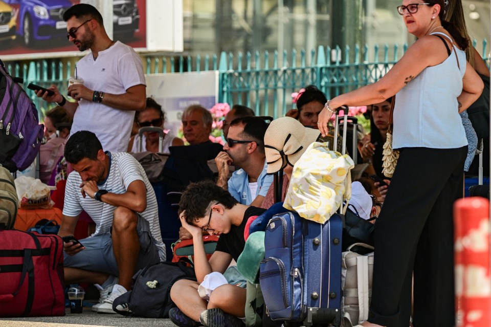 Travelers sitting on the ground at a port, waiting.