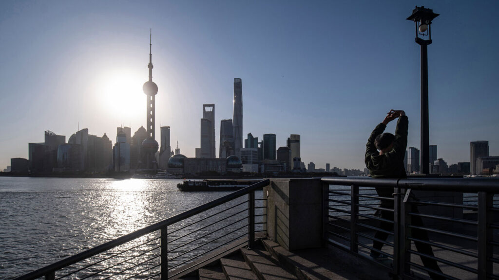 A man stretches out while exercising at sunrise on the Bund as skyscrapers of the Pudong Lujiazui Financial District stand across the Huangpu River, China.
